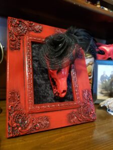 A piece I made of a red fox skull in a red frame. It had a black velvet background with a decorative black hat on. She also has eyelashes on, and crystals on her teeth